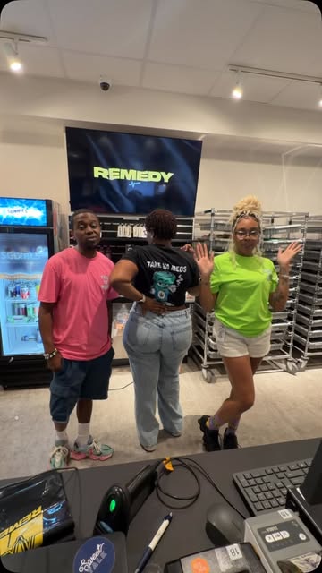 Three people at a dispensary, one wearing the black Take Ya Meds tee